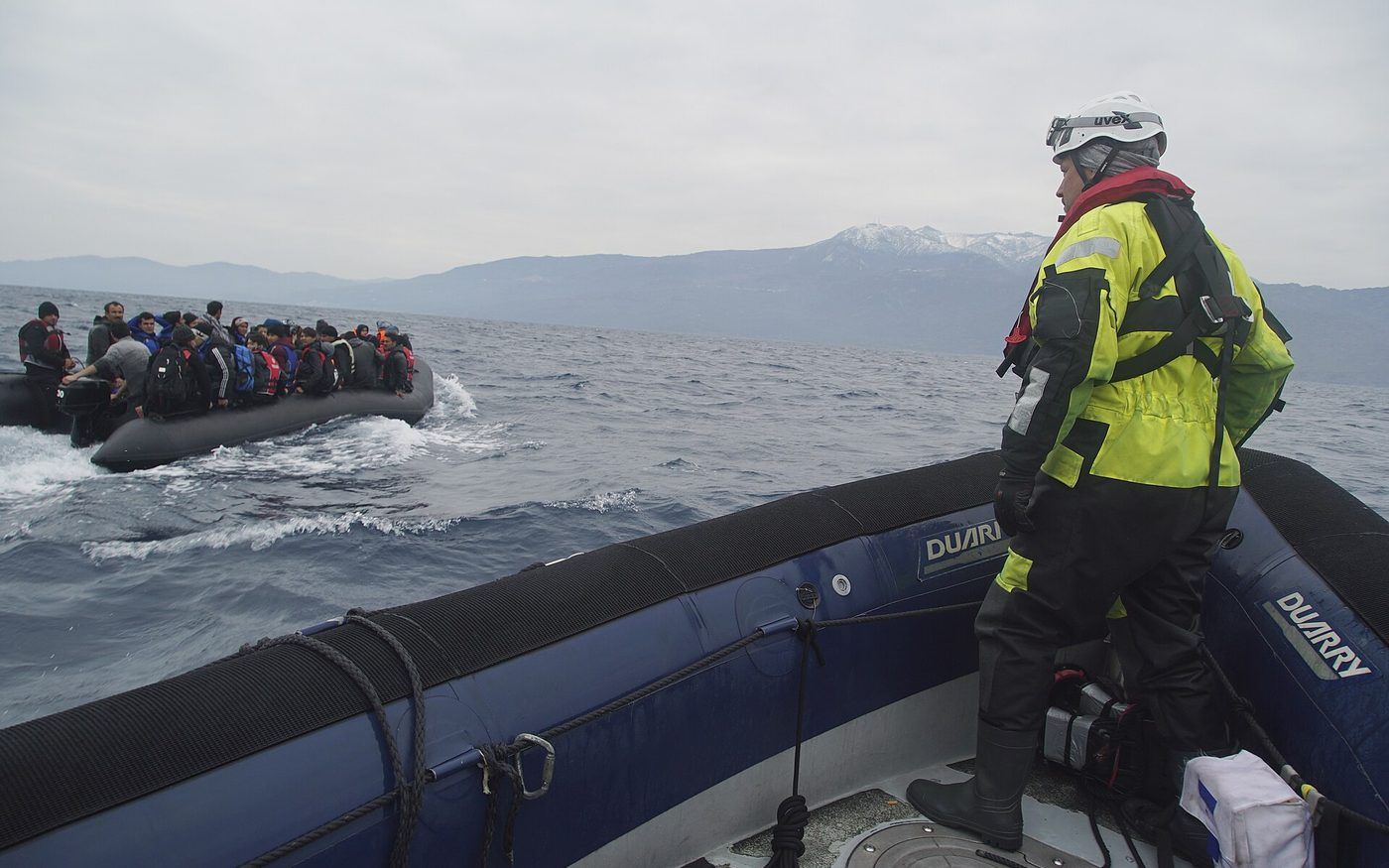 Ein überfülltes Schlauchboot mit Flüchtlingen auf dem Mittelmeer, im Vordergrund ein Retter